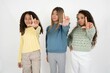 © Roquillo - beautiful multiracial kid girls  making fun of people with fingers on forehead doing loser gesture mocking and insulting.