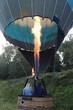 A group of people prepare a hot air balloon for flight using a gas burner and a fan.