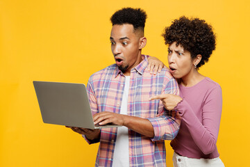 Wall Mural - Shocked sad scared young couple two friends family IT man woman wearing purple casual clothes together hold use work on laptop pc computer surfing internet isolated on plain yellow orange background.