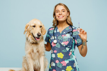 Wall Mural - Young veterinarian woman she wears uniform stethoscope heal exam hug embrace retriever dog do vaccine injection isolated on plain pastel light blue background studio portrait. Pet health care concept.