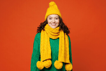 Wall Mural - Young smiling happy cheerful satisfied joyful woman she wearing green knitted sweater yellow hat scarf looking camera isolated on plain orange red color background studio portrait. Lifestyle concept.
