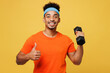 Young fitness trainer instructor sporty man sportsman wear orange t-shirt hold in hand dumbbell show thumb up spend time in home gym isolated on plain yellow background. Workout sport fit abs concept.