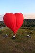 Heart shaped a hot air balloon flies with people over forests and fields in the morning at dawn