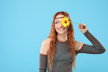 Wall Mural - Beautiful young hippie woman covering eye with sunflower on light blue background, space for text