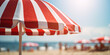 Close up of red and white striped sun parasol with blurry beach on sunny day in background