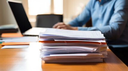 Wall Mural - Close-up of a man's hands typing on a laptop keyboard, with a stack of paperwork beside them