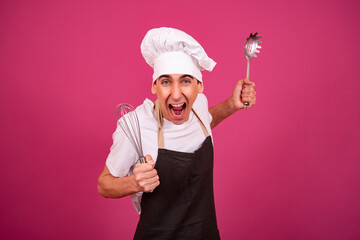 Young funny chef and pastry chef is cooking. Pink background.