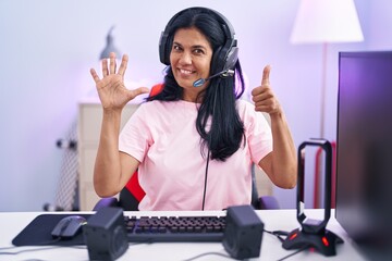 Sticker - Mature hispanic woman playing video games at home showing and pointing up with fingers number six while smiling confident and happy.