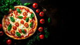 Fototapeta Dmuchawce - Delicious tasting Italian pizza with mozzarella cheese, cherry tomatoes and basil on top. resting on a black table, framed by cherry tomatoes and basil leaves seen from above. copy space