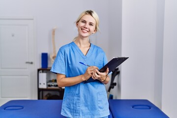 Wall Mural - Young blonde woman pysiotherapist smiling confident writing on document at rehab clinic