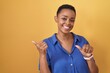 African american woman standing over yellow background pointing to the back behind with hand and thumbs up, smiling confident