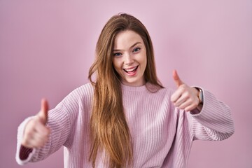 Poster - Young caucasian woman standing over pink background approving doing positive gesture with hand, thumbs up smiling and happy for success. winner gesture.