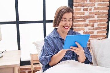 Poster - Middle age woman watching video on touchpad sitting on bed at bedroom