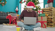 © Krakenimages.com - Young hispanic man using laptop drinking coffee celebrating christmas at home