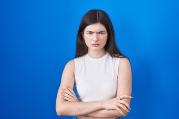 Sticker - Young caucasian woman standing over blue background skeptic and nervous, disapproving expression on face with crossed arms. negative person.