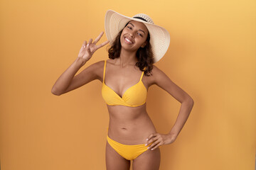 Poster - Young hispanic woman wearing bikini and summer hat smiling looking to the camera showing fingers doing victory sign. number two.