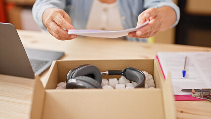 Sticker - Middle age hispanic woman ecommerce business worker packing headphones on package at office