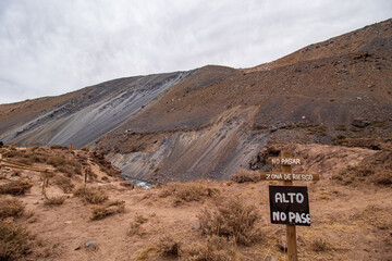 penhasco e uma placa de advertência escrita alto no pasa em  Cajón del Maipo e Embalse El Yeso, Chile