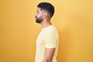 Poster - Hispanic man with beard standing over yellow background looking to side, relax profile pose with natural face and confident smile.