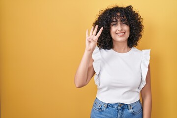 Poster - Young middle east woman standing over yellow background showing and pointing up with fingers number four while smiling confident and happy.