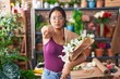 Asian young woman at florist shop holding bouquet of flowers pointing with finger to the camera and to you, confident gesture looking serious