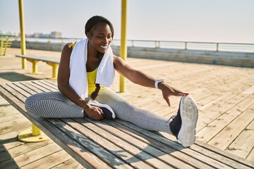 Sticker - African american woman wearing sportswear stretching leg at seaside