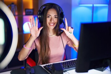 Sticker - Young hispanic woman playing video games showing and pointing up with fingers number seven while smiling confident and happy.