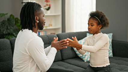 Wall Mural - African american father and daughter sitting on sofa playing hands game at home