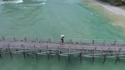 Canvas Print - Couple walking on pier, beach from drone with island and tropical holiday, waves and travel freedom in Indonesia. Ocean, vacation and relax, people on bridge at sea with aerial view of sand and water