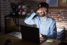 Young Hispanic Man With Beard Working At The Office At Night Smiling And Laughing With Hand On Face Covering Eyes For Surprise. Blind Concept.