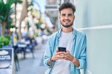 Wall Mural - Young hispanic man smiling confident using smartphone at street