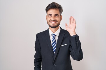 Poster - Young hispanic man with tattoos wearing business suit and tie waiving saying hello happy and smiling, friendly welcome gesture