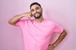 Hispanic young man standing over pink background smiling doing phone gesture with hand and fingers like talking on the telephone. communicating concepts.