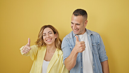 Poster - Man and woman couple standing together doing thumb up gesture over isolated yellow background