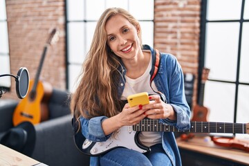 Poster - Young blonde woman musician playing electrical guitar using smartphone at music studio