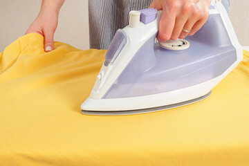 Wall Mural - Girl ironing clothes with an iron on an ironing board selective focus