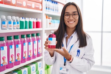 Canvas Print - Young hispanic woman working at pharmacy drugstore holding syrup smiling with a happy and cool smile on face. showing teeth.