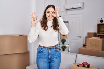 Sticker - Young hispanic woman holding keys of new home smiling happy doing ok sign with hand on eye looking through fingers