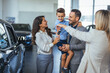 © Dragana Gordic - Young happy family enjoying while buying a new car in a showroom. Saleswoman at car dealership center helping family to choose new family vehicle. Family in a car dealership