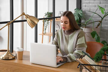 Young woman using laptop at table in office