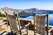 Rocking chairs overlooking the rim of the caldera with Wizard Island in the background in Crater Lake National Park, Oregon United States on a clear summer day.