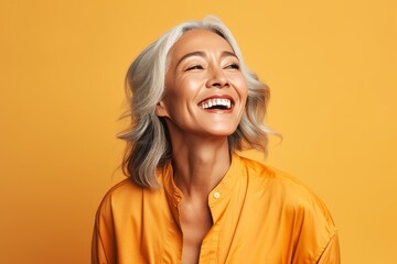 Portrait of happy senior woman in yellow shirt over yellow background.