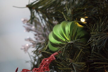 Green swirl ornament illuminated by yellowish-white Christmas lights on fake pine tree, star in background