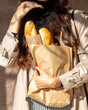 The girl holds a bag of bread baguettes in her hands