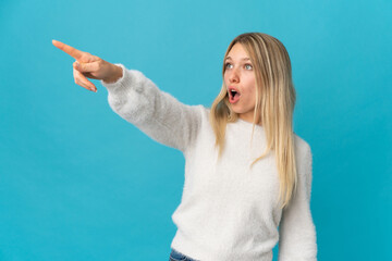 Poster - Young blonde woman isolated on blue background pointing away