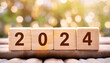 Four wooden blocks in a row saying 2024 on a wooden table, with a blurry fairy lights bokeh background. Holidays New Year 2024 concept.	