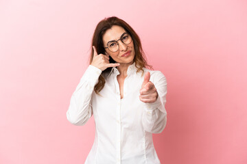 Wall Mural - Middle aged caucasian woman isolated on pink background making phone gesture and pointing front