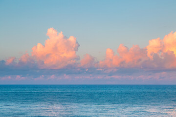 Poster - Fluffy pink clouds over a calm sea at dawn.