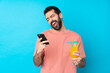 © luismolinero - Young man over holding a cocktail over isolated blue background with phone in victory position
