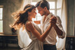 © VisualProduction - Man and woman dancing. Couple practicing first wedding dance, partners focused on each other, both dressed in white on black background.